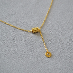Vue détaillée d'un collier plaqué or avec pendentif cylindrique texturé et petit anneau