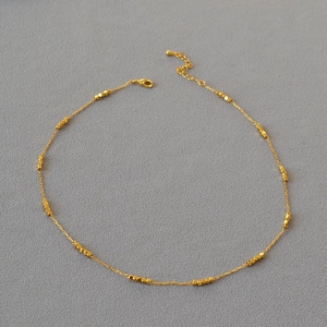 Close-up of gold-plated brass necklace with faceted square beads on flat grey texture