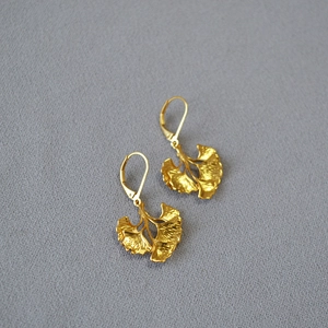 Macro detail of gold-plated ginkgo leaf earrings showing intricate texture and lever back hooks