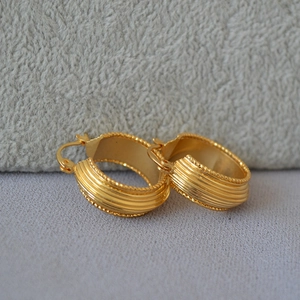 Macro shot of French vintage gold-plated hoop earrings with striped texture and milgrain edge