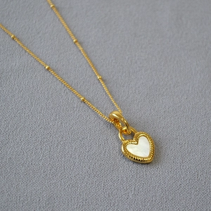 Détail macro du pendentif cœur doré avec nacre blanche sur une chaîne à perles élégante