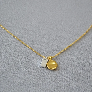 Close-up of gold and silver contrast pendants with brass plated chain and bean detail