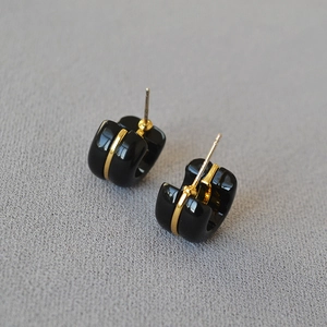 Macro shot of black acrylic C-shaped earrings with embedded vertical gold metal stripe