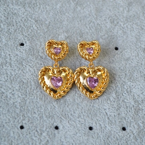 Macro detail of gold-plated heart earrings with pink zircon and twisted rope borders