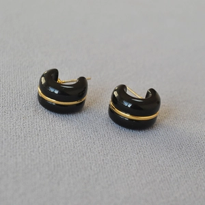 Macro detail of glossy black C-shape earrings with a sleek gold-tone center line detail