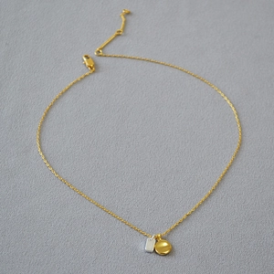Detailed flat lay of two-tone geometric pendant necklace on gray textured background