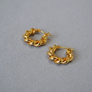 Gros plan de boucles d'oreilles créoles torsadées plaquées or sur tissu texturé gris