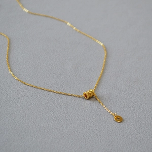 Détail du collier en laiton doré avec pendentif cylindrique texturé minimaliste
