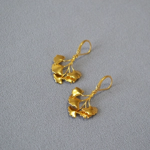 French vintage matte gold ginkgo leaf earrings on grey textured fabric background