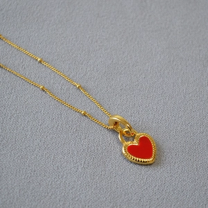 Gros plan d'un collier doré avec pendentif cœur en émail rouge sur fond gris texturé