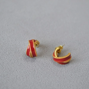 Macro detail of vintage ribbon-shaped gold-plated earrings with red enamel and beaded trim