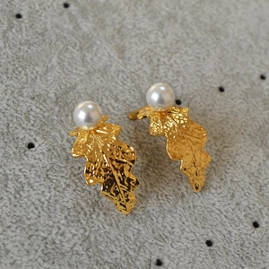 Close-up of golden leaf earrings showing irregular leaf texture and white pearl detail