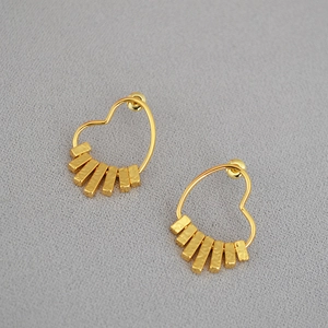 Golden heart-shaped dangle earrings with hammered rectangular charms on grey fabric