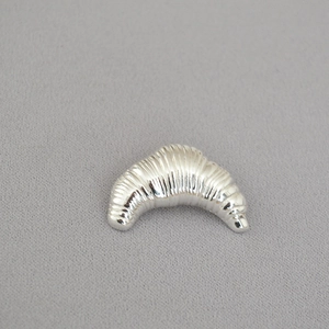 Detailed view of silver croissant-shaped brooch with textured metallic finish on fabric