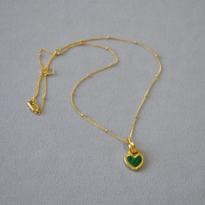 Détail d'un pendentif cœur vintage avec malachite verte et bordures perlées dorées