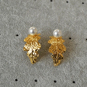 Detail of gold-plated leaf earrings with hammered texture and white pearl accents