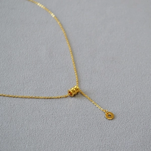 Vue détaillée du pendentif cylindre plaqué or avec texture rainurée sur une chaîne en O