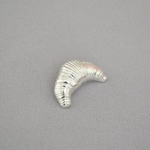 Detailed close-up of a silver croissant shaped brooch with realistic textured metal finish
