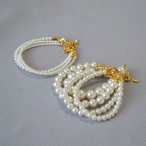 Détail de bracelets en perles blanches multicouches avec fermoirs dorés et chaîne réglable