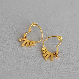 Detail view of heart-shaped gold dangling earrings featuring hammered rectangular bars