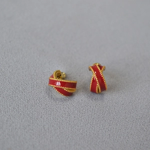 Detailed close-up of red enamel twisted cross earrings with delicate golden beaded edges
