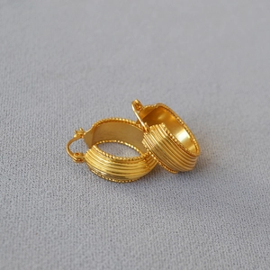 Close-up of vintage gold-plated brass earrings with ribbed texture and beaded edges
