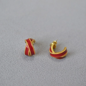 Close-up of C-shaped gold-plated earrings with red enamel and beaded vintage textures