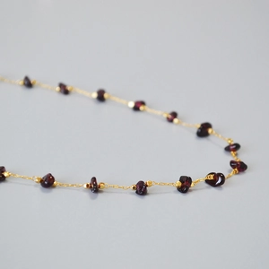 Macro detail of gold necklace featuring irregular deep red garnet stones and small beads