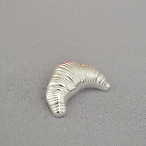 Macro shot of silver croissant-shaped brooch showing detailed metallic spiral textures