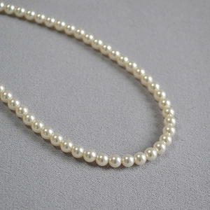 Collier élégant à un rang de perles crème sur fond texturé gris