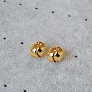 Detailed view of polished gold plated C-shape earrings on a textured background