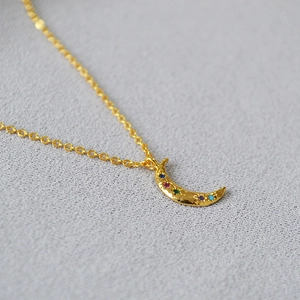 Macro detail of gold moon necklace with hammered texture and colorful gemstones