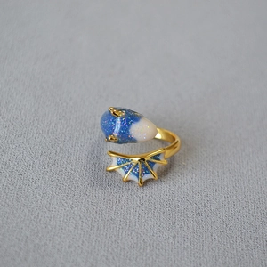 Adjustable gold dragon ring with blue and white enamel wings on a grey fabric background