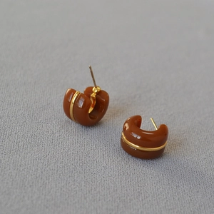 Caramel brown C-shaped hoop earrings with gold trim and polished finish on gray fabric