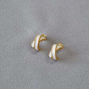 Detail of cross-shaped gold earrings with white enamel and beaded edging texture