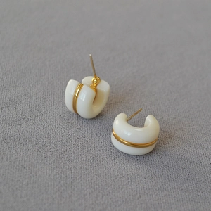 Detail of white C-shaped hoop earrings with a gold metal band on a gray fabric base