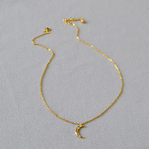 Close-up of gold moon necklace with colorful zircon stones on a grey background