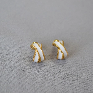 Close-up of cross-shaped enamel stud earrings with gold beaded edges on a gray base