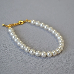 Détail d'un bracelet en perles blanches avec fermoir mousqueton doré et chaîne réglable
