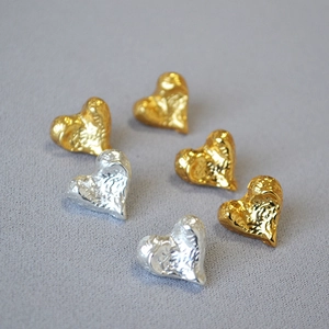Detailed close-up of textured heart earrings in gold and silver finish with lava texture