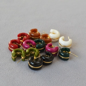 Flat lay of colorful C-shaped resin hoop earrings with elegant gold metallic accents