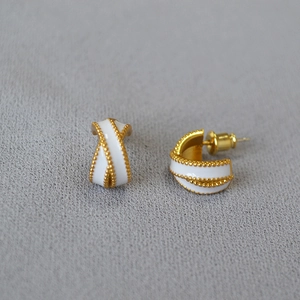 Detailed close-up of gold-plated brass earrings with white enamel and beaded edge details