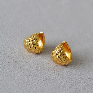 Macro detail of gold-plated spherical hoop earrings with textured relief patterns