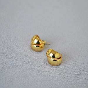 Detailed view of polished gold bean stud earrings on a textured grey fabric background