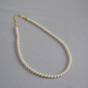 Détail d'un collier de perles blanches avec fermoir mousqueton doré et chaîne réglable