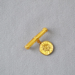Detailed close-up of gold coin brooch featuring Medusa relief on gray fabric background