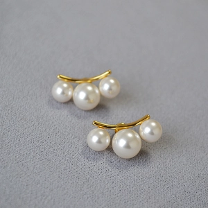 Détail de boucles d'oreilles en laiton doré avec perles blanches sur tissu gris