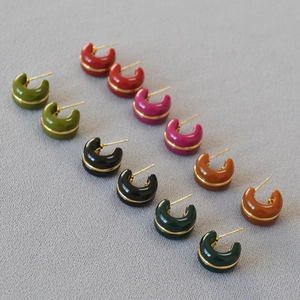 Detail view of colorful C-shaped hoop earrings with gold line inlay on grey fabric