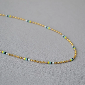 Ras du cou minimaliste en perles colorées et tubes en laiton doré sur fond gris texturé
