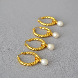 Boucles d'oreilles créoles dorées torsadées avec perles d'eau douce sur fond gris